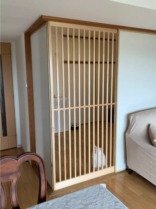 猫対策として特注木製障子をリビング横に配置した例。部屋中に座る白猫の様子。こちらを見ています。