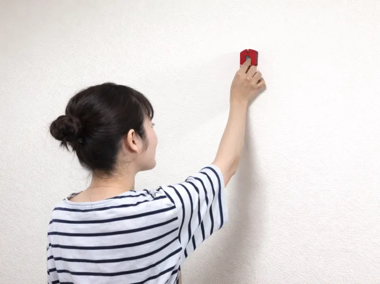 壁の下地を探すために下地センサーを使って測定している女性