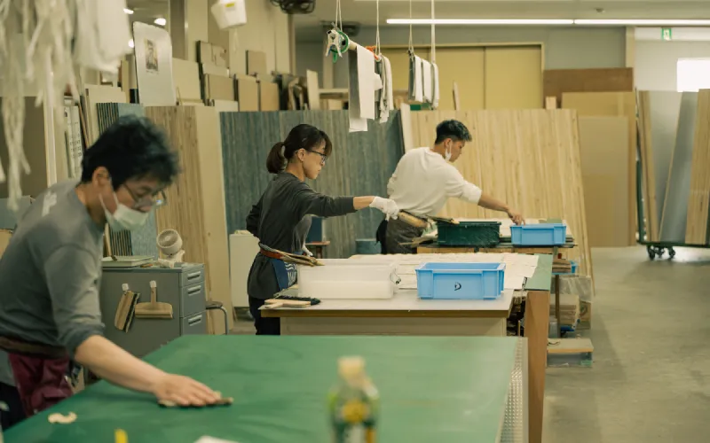 工房内で複数の職人が広い作業台を使い、それぞれの作業に集中している様子