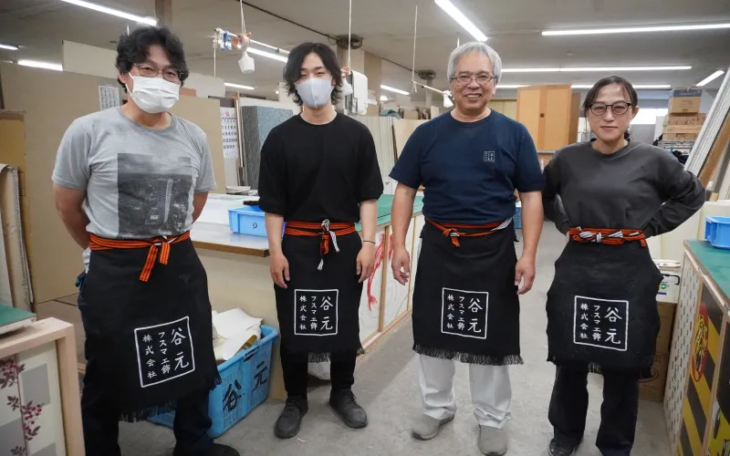 工房内で「谷元」と書かれたエプロンを着用した4人の職人たちが並んで撮影された集合写真