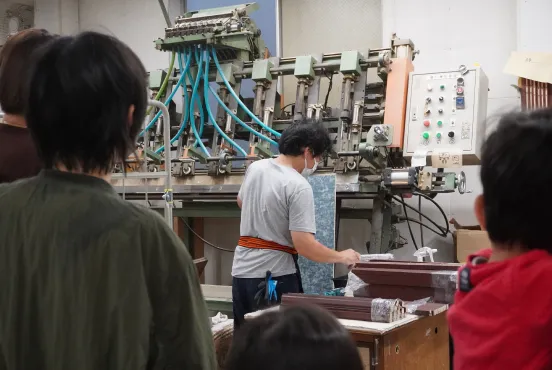 大型の機械の前で作業を行う職人の背中を撮影した工房内の様子