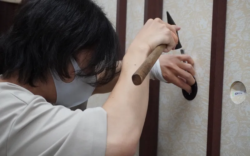 マスクを着用した職人が、木槌を使って建具に金具を取り付けている作業の様子